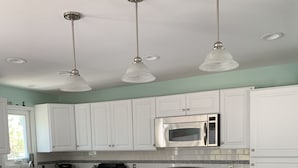 Una cocina moderna con armarios blancos, encimera de granito, estufa de acero inoxidable y microondas. Hay dos sillas de madera con cojines rojos en la isla.