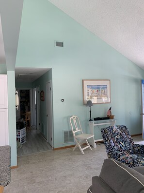 Un salon avec un mur bleu clair, un fauteuil blanc, un canapé foncé et un tableau encadré accroché au-dessus d’un bureau.