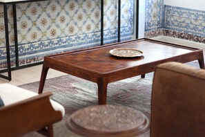 Uma mesa de centro de madeira com um prato decorativo em um quarto com paredes de azulejos estampados e piso coberto por carpete.