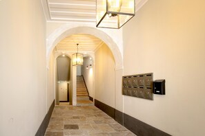 A hallway with a stone floor, an arched doorway, a staircase, and a wall-mounted mail slot. - Nomad s Downtown Lisbon - 3bdr Charming Memory (Lisbon)