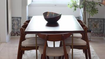 Een eettafel met een donkere kom, omringd door houten stoelen met beklede zitplaatsen, in een kamer met betegelde muren en een raam.