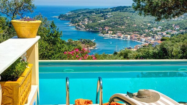 A pool with a view of a coastal town, a lounge chair, and a potted plant. - Theodora Villa - 2 BR Tranditional House Close to Gaios Town (Paxos)