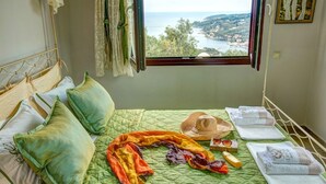 A bedroom with a view of a coastal landscape, a bed with green bedding, pillows, a hat, and toiletries. - Theodora Villa - 2 BR Tranditional House Close to Gaios Town (Paxos)