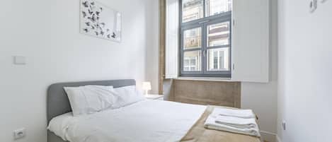 A modern bedroom with a bed, a window, and a wall-mounted artwork.