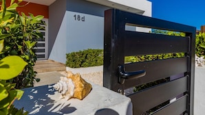 Un edificio moderno con un portón negro, el número '18d' en la pared, y una concha marina en el suelo.