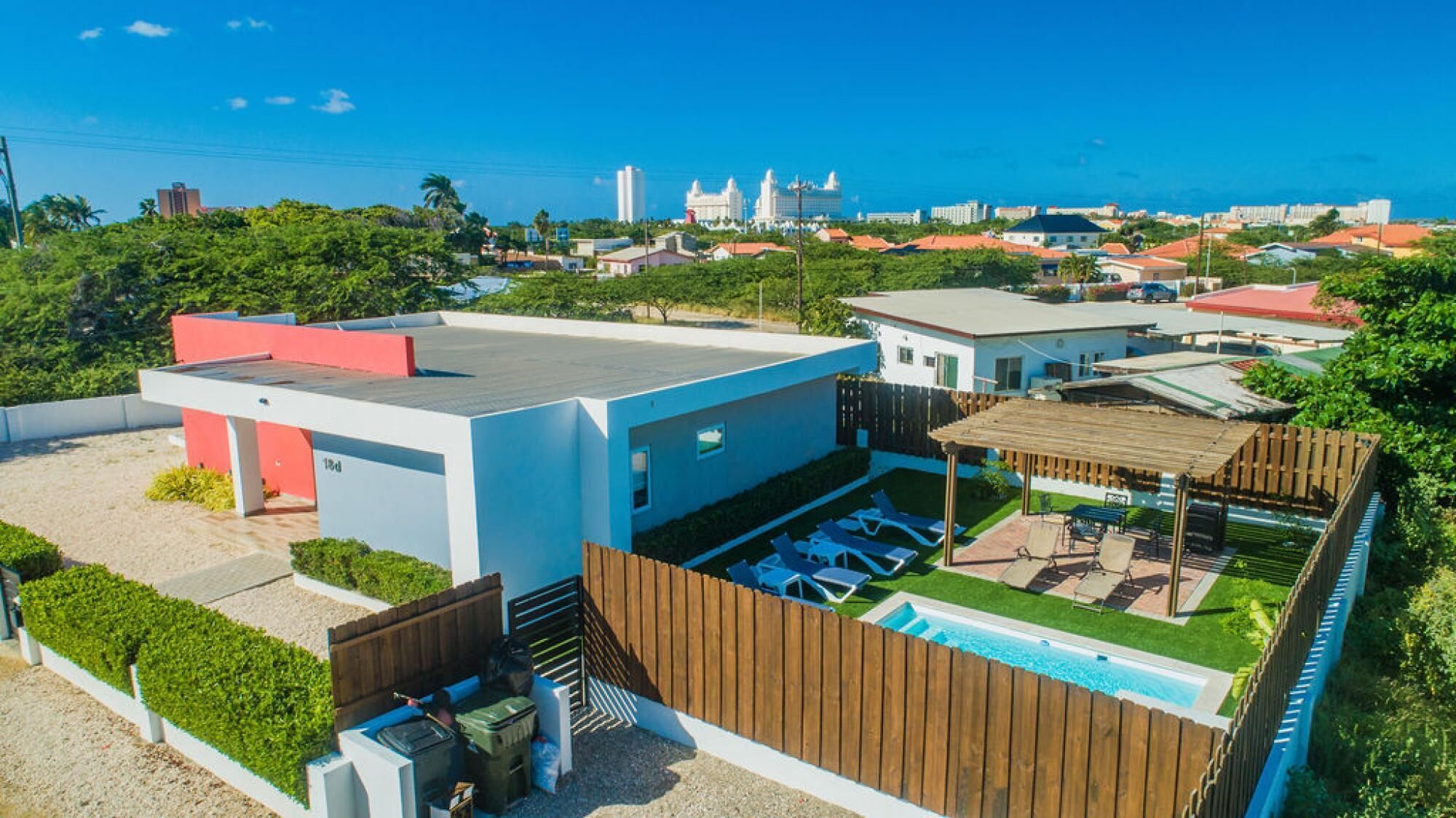 Ett modernt hus med en pool på taket, en inhägnad trädgård och utsikt över havet och stadens silhuett.