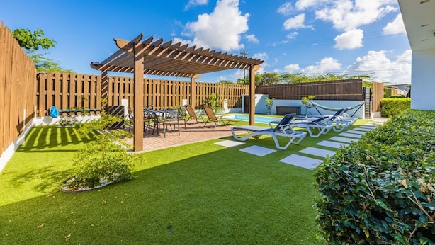 Un patio trasero con una pérgola de madera, una piscina y sillas de descanso.