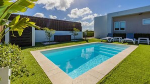 Una piscina rodeada de un césped cuidado, con un cerco de madera y un edificio moderno al fondo.