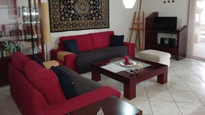 A living room with a red sofa, a grey sofa, a coffee table, a TV stand, and a large decorative rug. - Kallithea Comfy 1 in Kalithea (Kallithea)