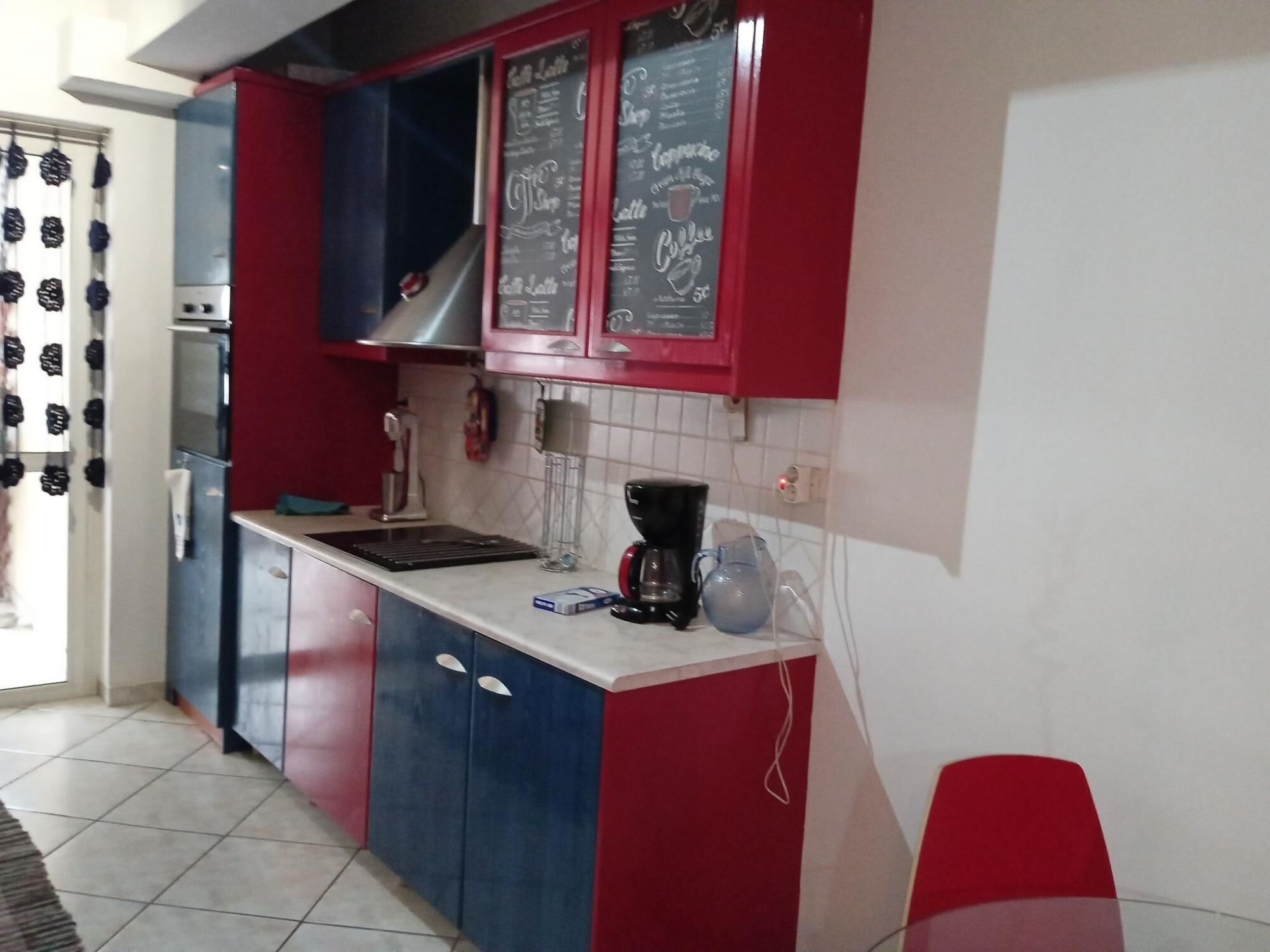 A kitchen with red and blue cabinets, a coffee maker, and a kettle on the counter.