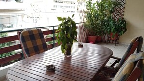 A wooden table with two chairs, a potted plant, and a small incense holder on a balcony with a view of buildings. - Kallithea Comfy 1 in Kalithea (Kallithea)