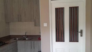 Een kleine keuken met houten kastjes, een spoelbak en een prullenbak.
