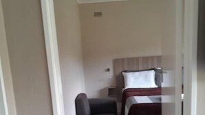 Een smalle gang die leidt naar een slaapkamer met een bed, nachtkastje en een zithoek.