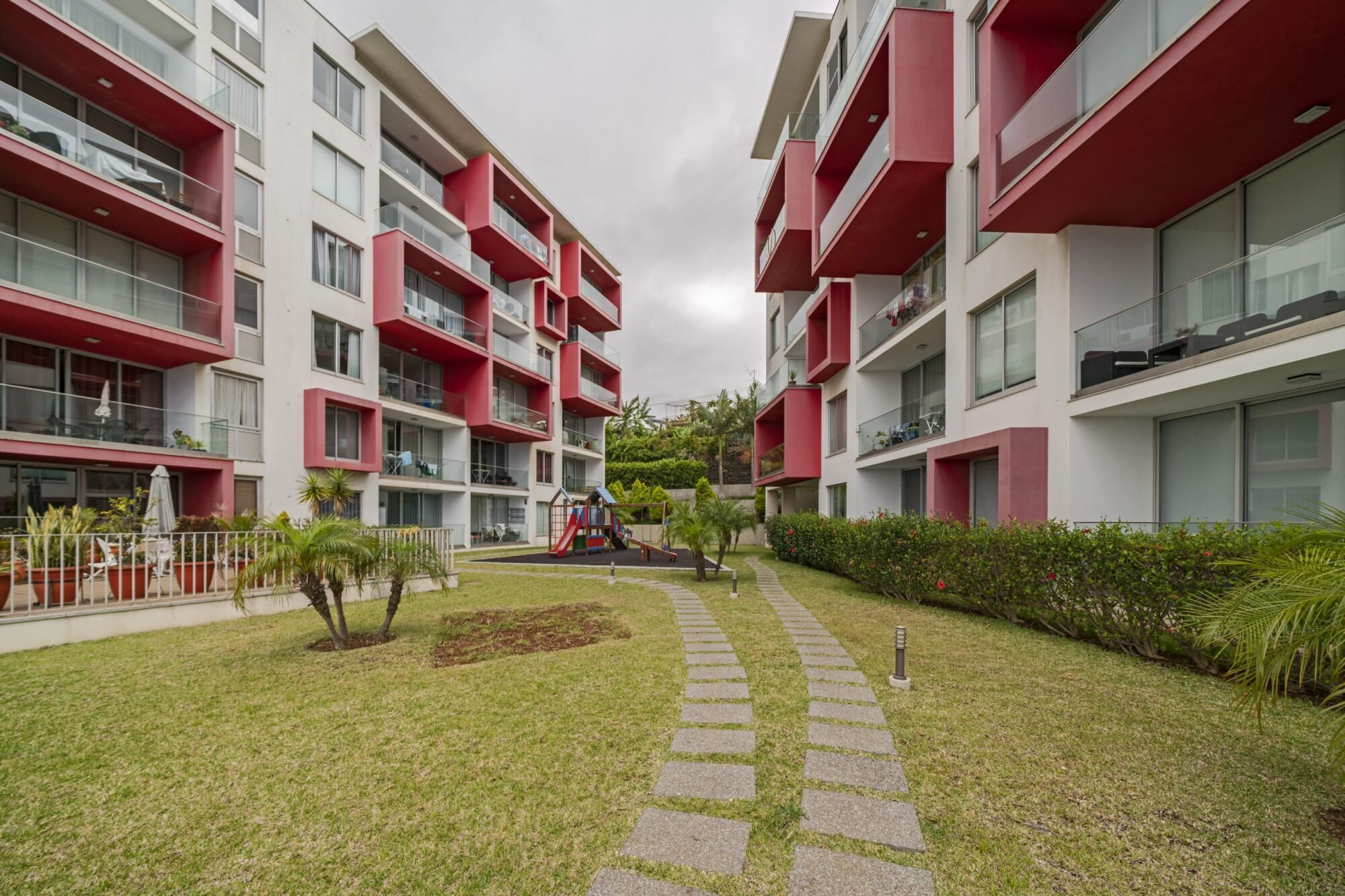 Een modern appartementencomplex met rode balkons en een centrale binnenplaats met een speeltuin.