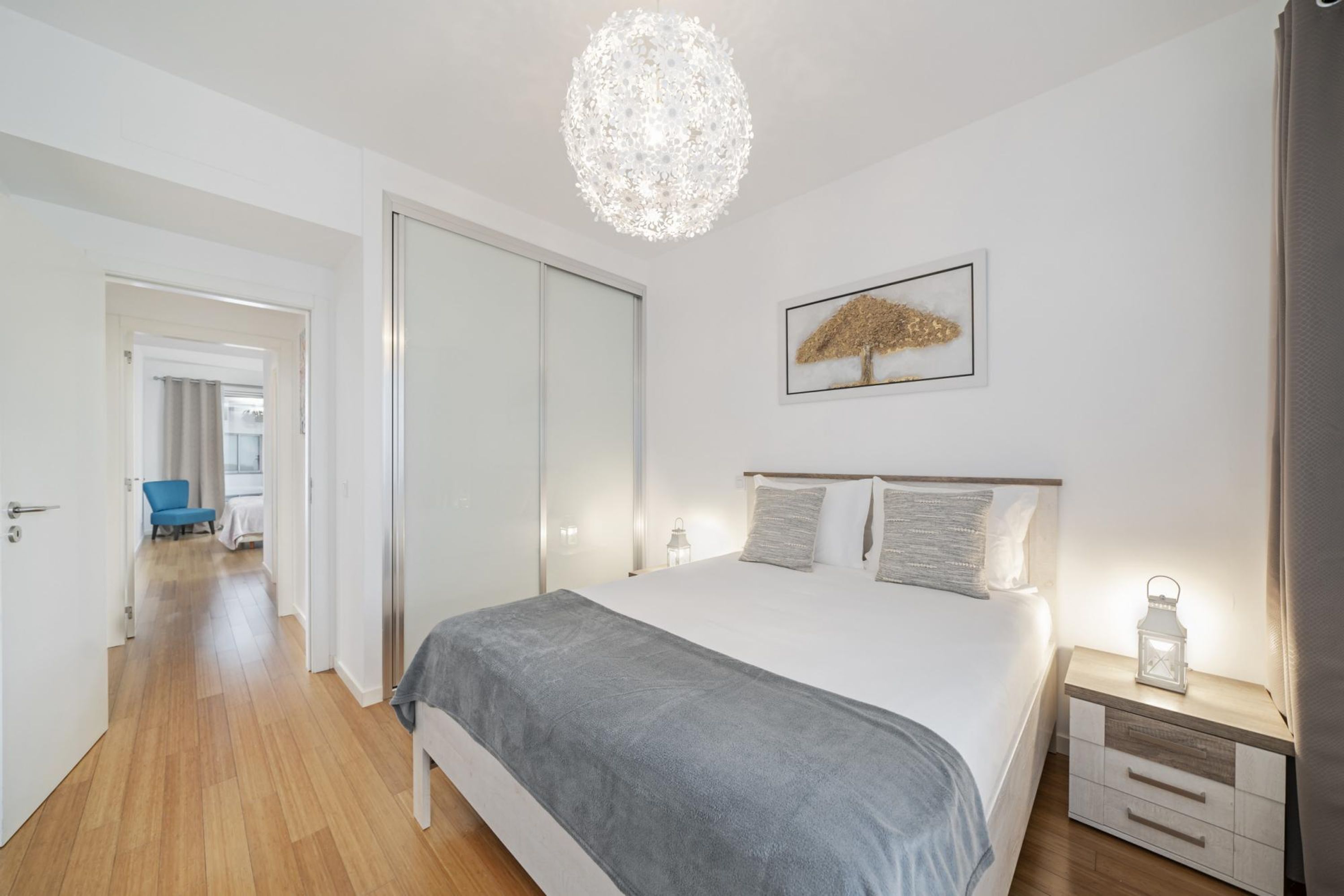 A modern bedroom with a large bed, bedside tables, a chandelier, and a framed picture on the wall.