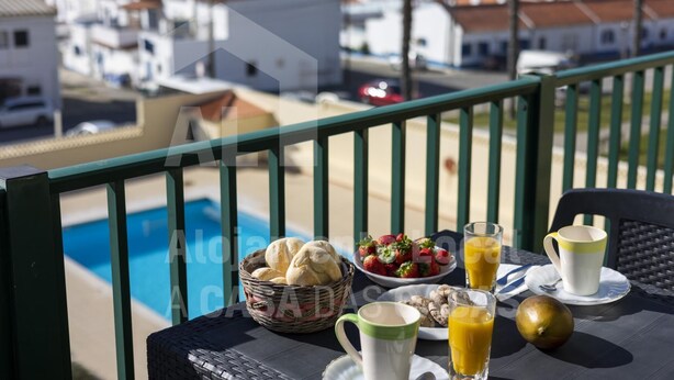 Ein Balkon mit Frühstückstisch, Blick auf einen Pool und die Küste.