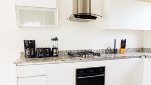 A modern kitchen with white cabinets, a built-in oven, a gas stove, a coffee maker, a toaster, and a blender. - Residences C2-pbb in Chame (Punta Chame)