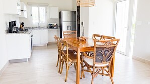 A modern kitchen with white cabinetry, a dining table with wicker chairs, and a hanging light fixture. - Residences C2-pbb in Chame (Punta Chame)
