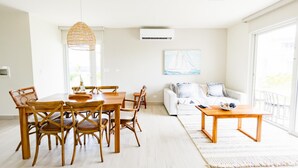 A bright living room with a dining area, featuring a wooden dining table, wicker chairs, a white sofa, and a large window. - Residences C2-pbb in Chame (Punta Chame)