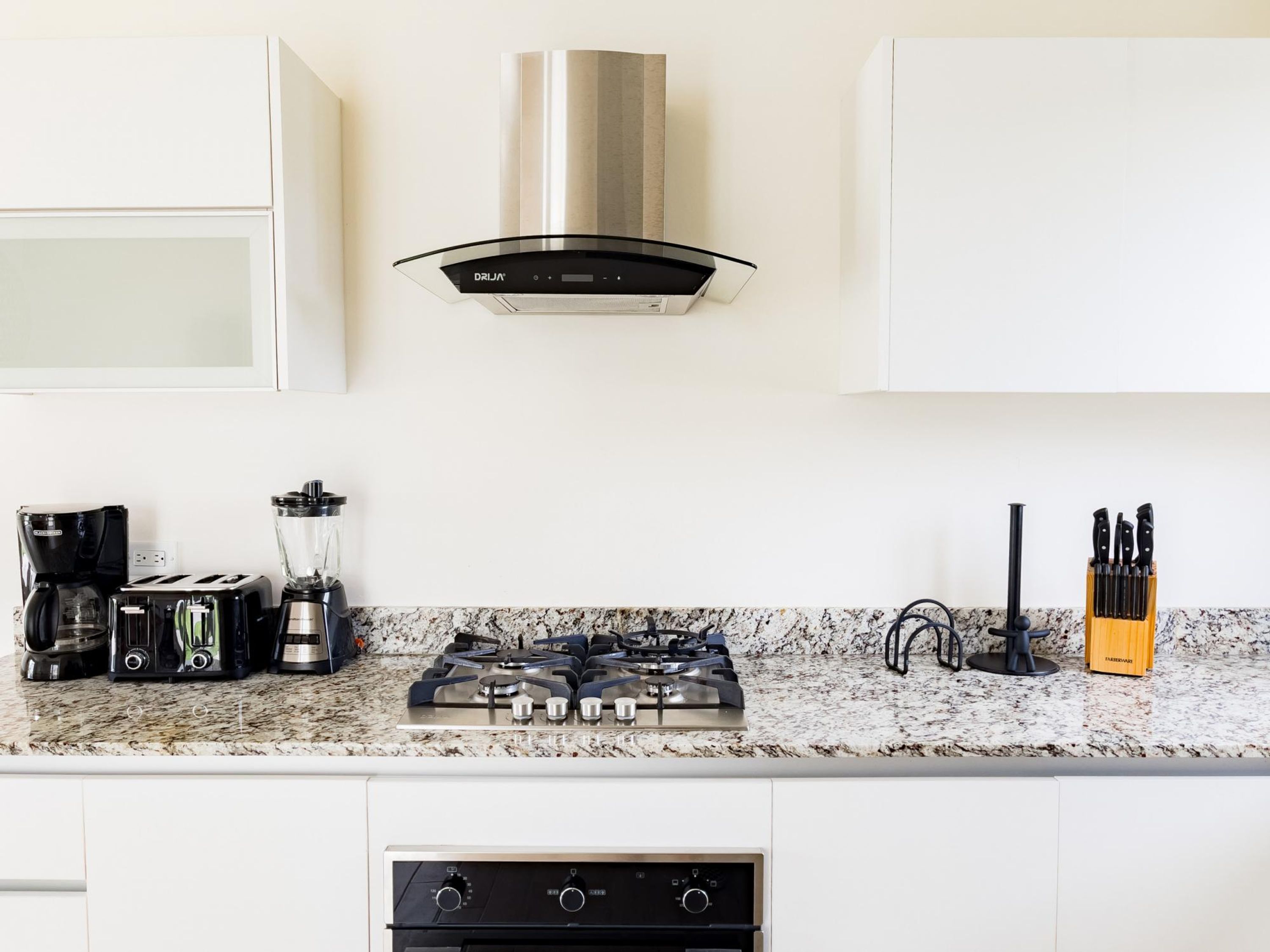 Una cocina moderna con estufa a gas, cafetera, tostadora y licuadora.