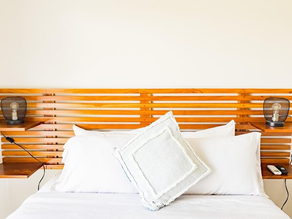 A neatly made bed with white linens, a white pillow, and a white towel. There are two black wall-mounted lamps on either side of the bed.