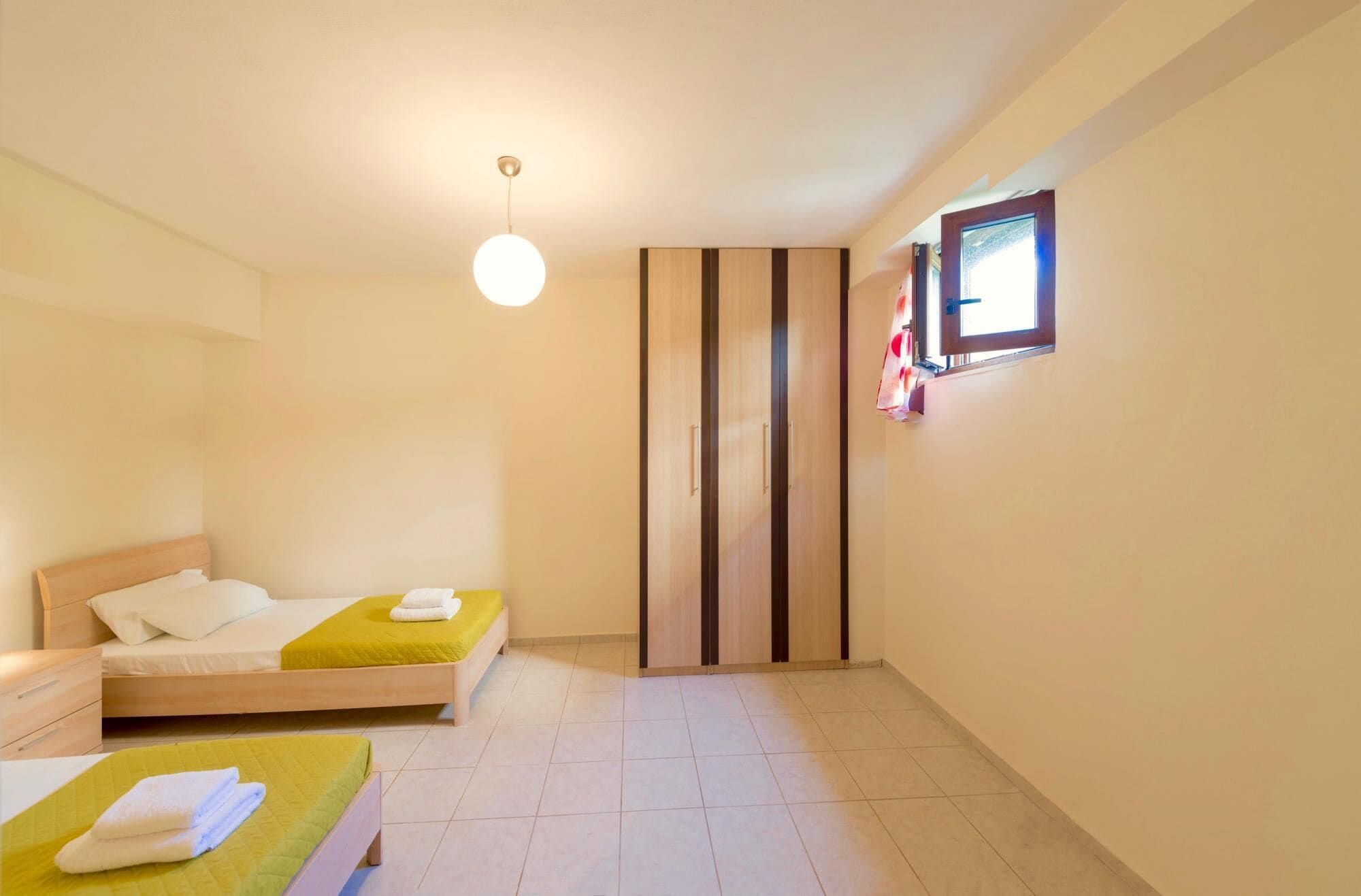 A bedroom with two beds, a wardrobe, a small window, and a hanging light fixture.