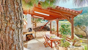 Een terras buiten met een houten pergola, stenen muren en een barbecueplek.
