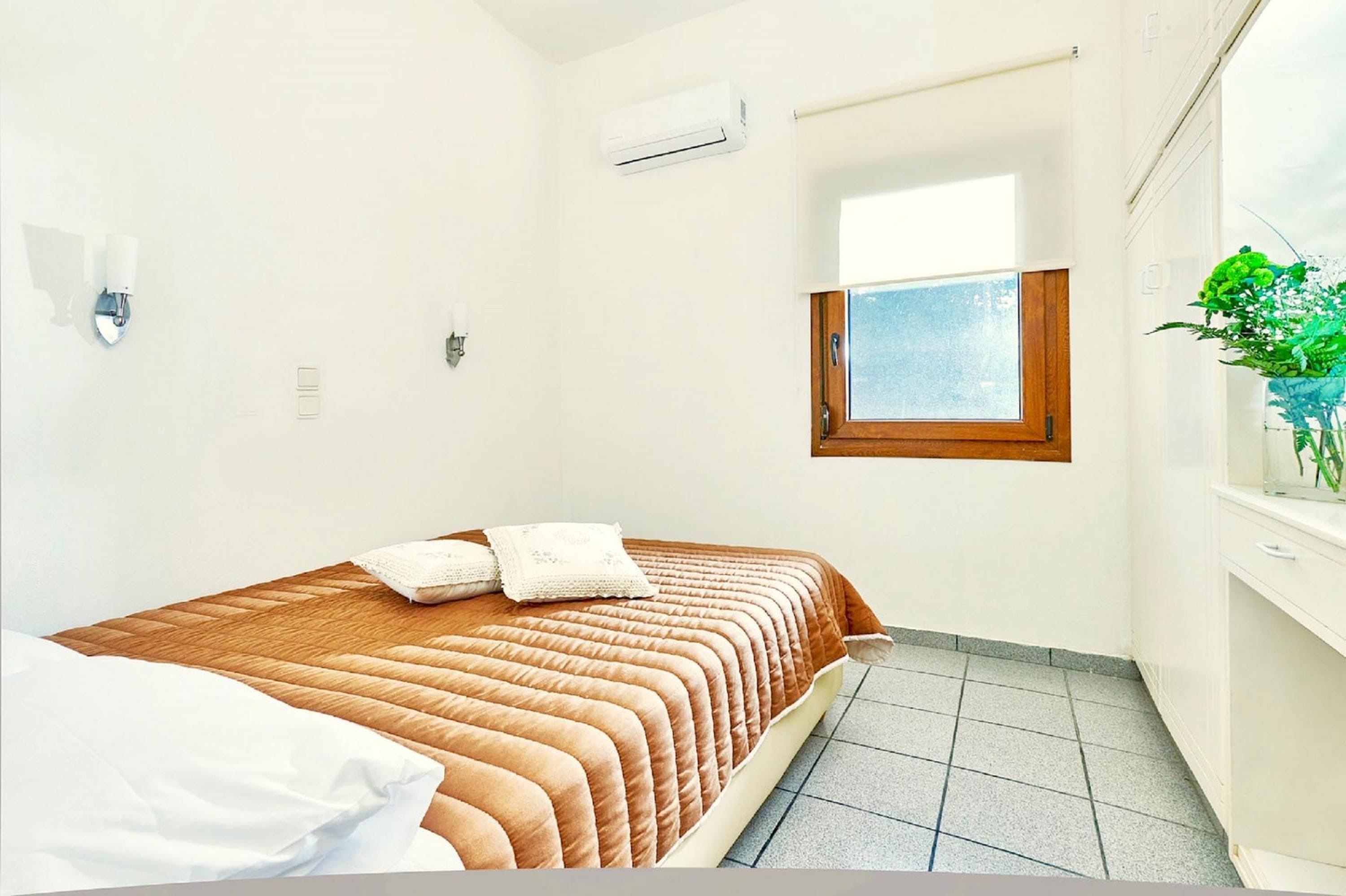 Ein Schlafzimmer mit Bett, Fenster, Klimaanlage und einer Pflanze.