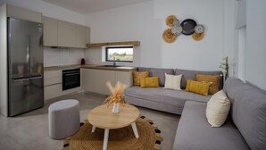 Eine moderne Küche mit integriertem Kühlschrank, Backofen und Geschirrspüler. Ein graues Sofa mit gelben Kissen und ein runder Couchtisch mit einer Vase.