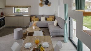 Eine moderne Küche mit Einbauofen, ein Essbereich mit Tisch für zwei Personen und ein graues Sofa mit Zierkissen.