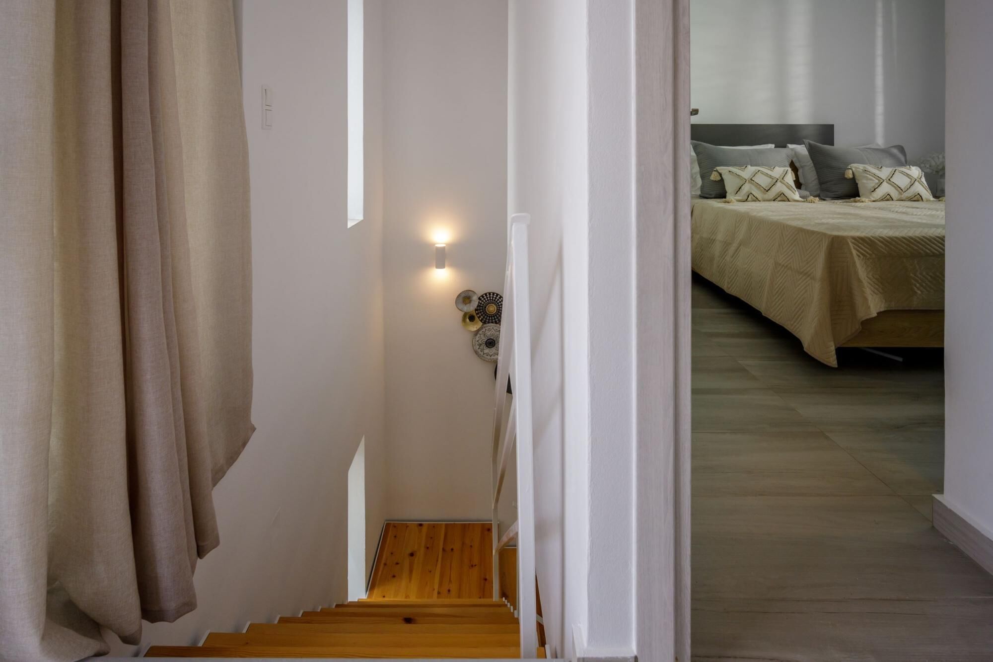 A staircase leading to a bedroom with a bed, pillows, and a wall-mounted light fixture.