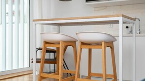 Una cocina moderna con mostrador de madera, dos taburetes blancos y vistas al exterior a través de amplias ventanas.