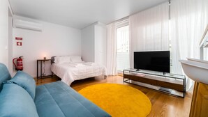 Un dormitorio moderno con cama, televisor, sofá y alfombra amarilla.