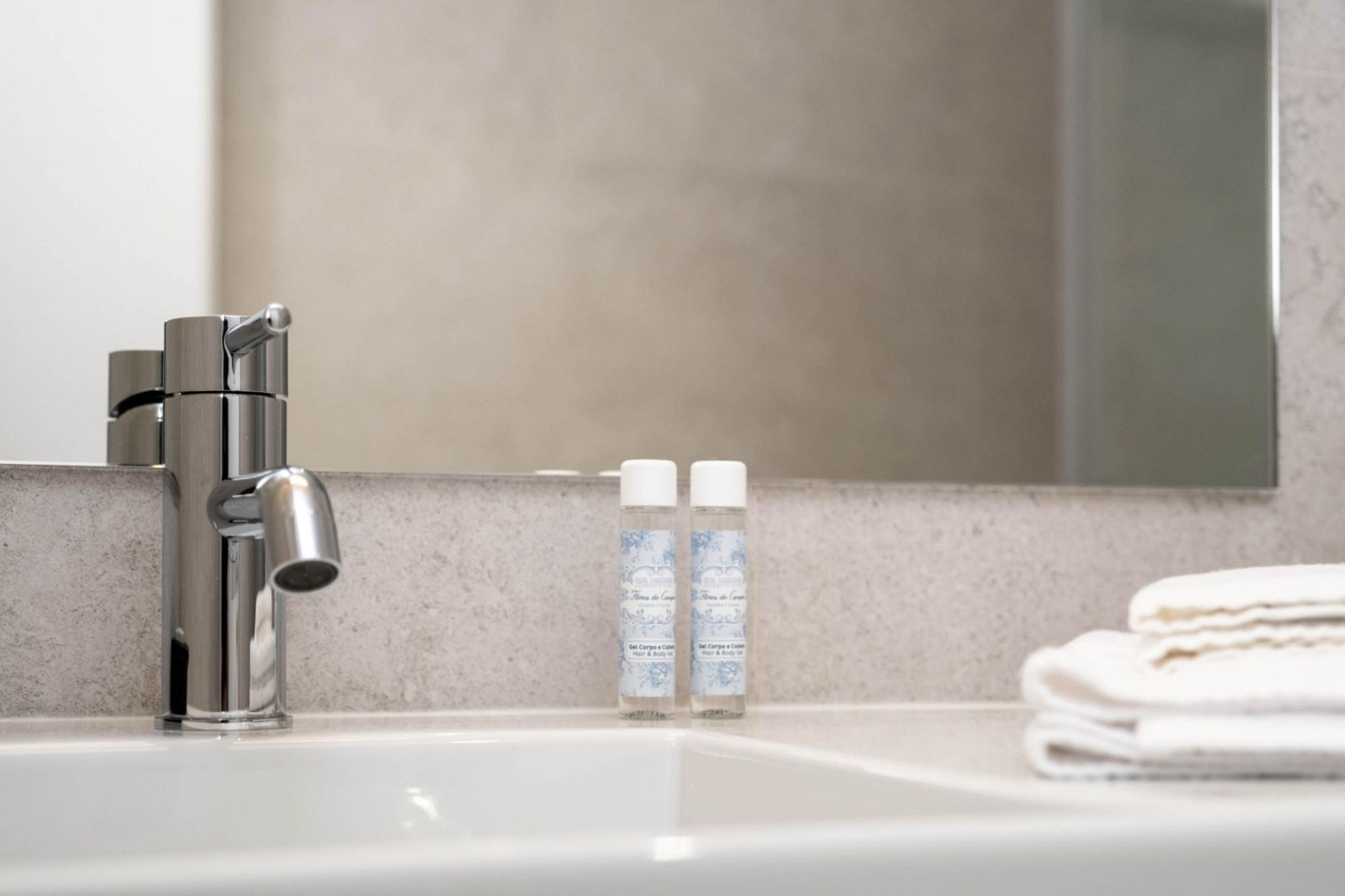 Un lavabo de salle de bain avec un robinet moderne, deux flacons de savon liquide et une pile de serviettes pliées.