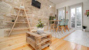 A room with a stone wall, wooden furniture, a TV mounted on the wall, and a view through a glass door.