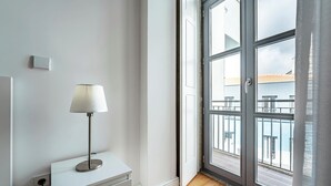 A modern room with a white dresser, a lamp, and a large window with a view of buildings. - Nomad s Formosa Harmony - 1bed Porto (Porto)