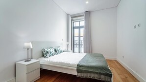 A bedroom with a bed, bedside tables, a window with curtains, and a wooden floor. - Nomad s Formosa Harmony - 1bed Porto (Porto)