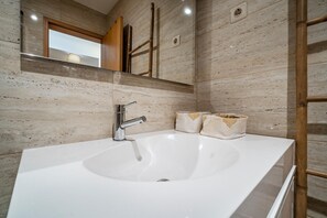 Ein Badezimmer mit einem großen, weißen Waschbecken, einem Spiegel und einer Holzlade.