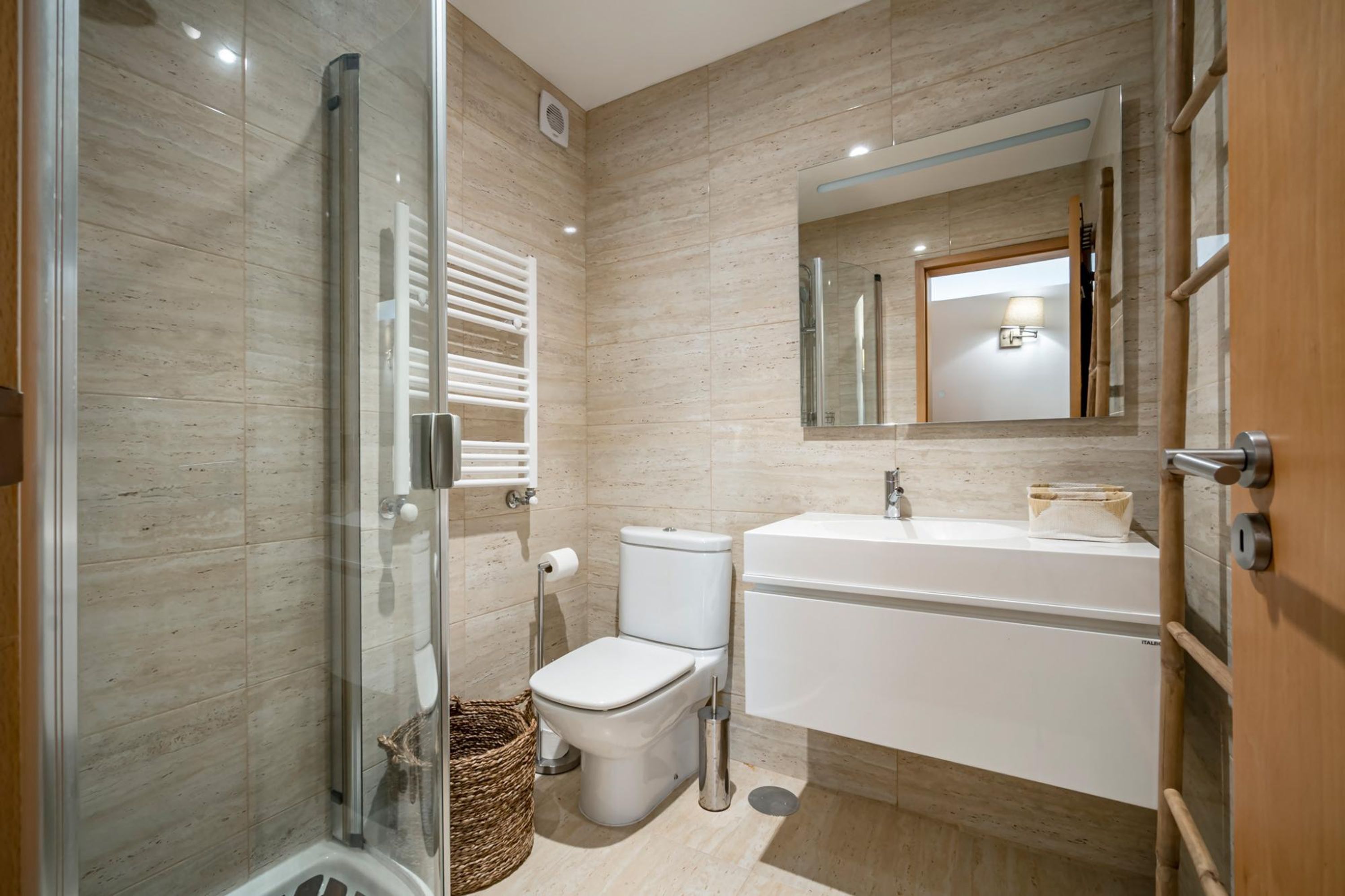 Ein modernes Badezimmer mit Duschkabine aus Glas, Toilette, Waschbecken und Spiegel.