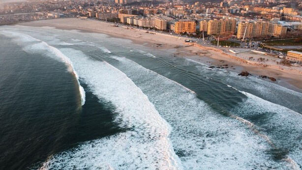 An aerial view of a coastal city with a beach, buildings, and a marina.