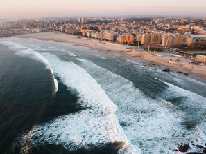Vue aérienne d’une ville côtière avec une plage, des bâtiments et un port de plaisance.