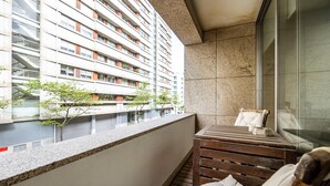 A balcony with a wooden bench, a small table, and a view of a high-rise building.
