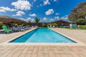 Relax by the pool surrounded by lush greenery and a thatched-roof cabana.