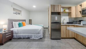 A modern hotel room with a bed, bedside table, and a kitchenette area including a refrigerator and microwave. - Turibana Plaza Suite 10 (Noord)