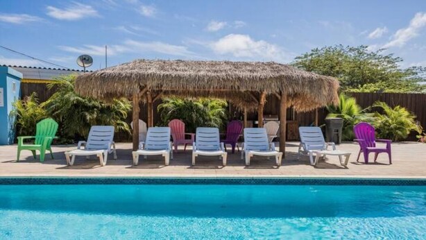 A swimming pool with lounge chairs and a thatched-roof structure. - Turibana Plaza Suite 10 (Noord)