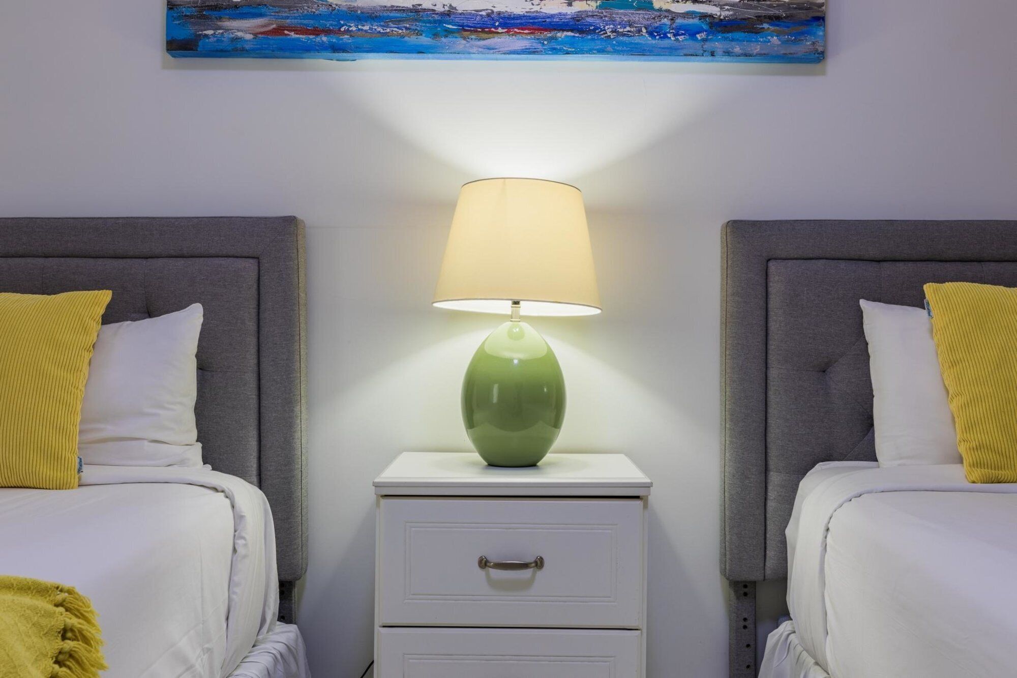 A hotel room with two beds, a nightstand with a lamp, and a painting on the wall.