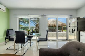A modern kitchen with a refrigerator and a dining area with a glass table and chairs. - Koyari Modern Condos 2 (Noord)
