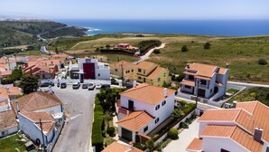 A coastal residential area with houses featuring red-tiled roofs, a paved road, and a view of the sea. - Villa Octopus s Garden by Acasadascasas (Mafra)