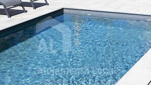 Ein rechteckiger Swimmingpool mit klarem, blauem Wasser, umgeben von einer gefliesten Terrasse.