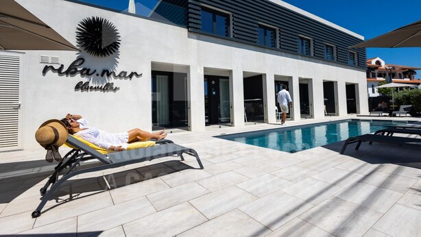 Ein modernes Gebäude mit Poolbereich, einer Liege und einer Person, die am Pool entspannt.